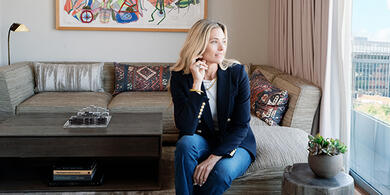 Veronica Beard, dressed in a navy blazer, stands in a suite at The Dupont Circle Hotel, looking out the window as part of "The Blazer Library" offer introduction.