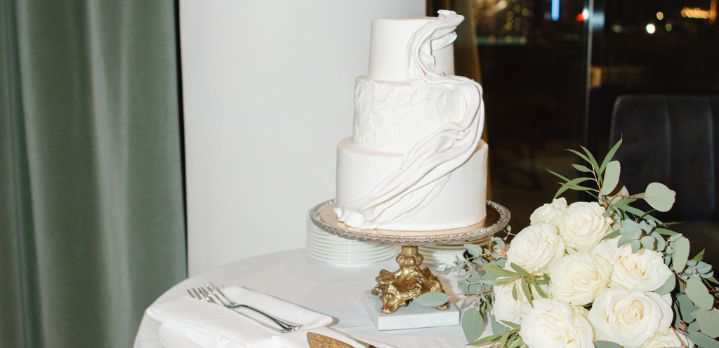A classic multi-tiered white wedding cake displayed on a decorated table at a Glover Park reception in The Dupont Circle Hotel