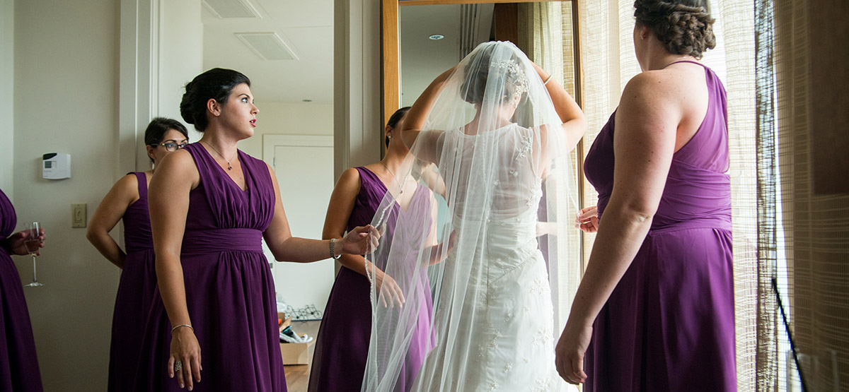 Bride adjusting her veil with bridesmaids looking on