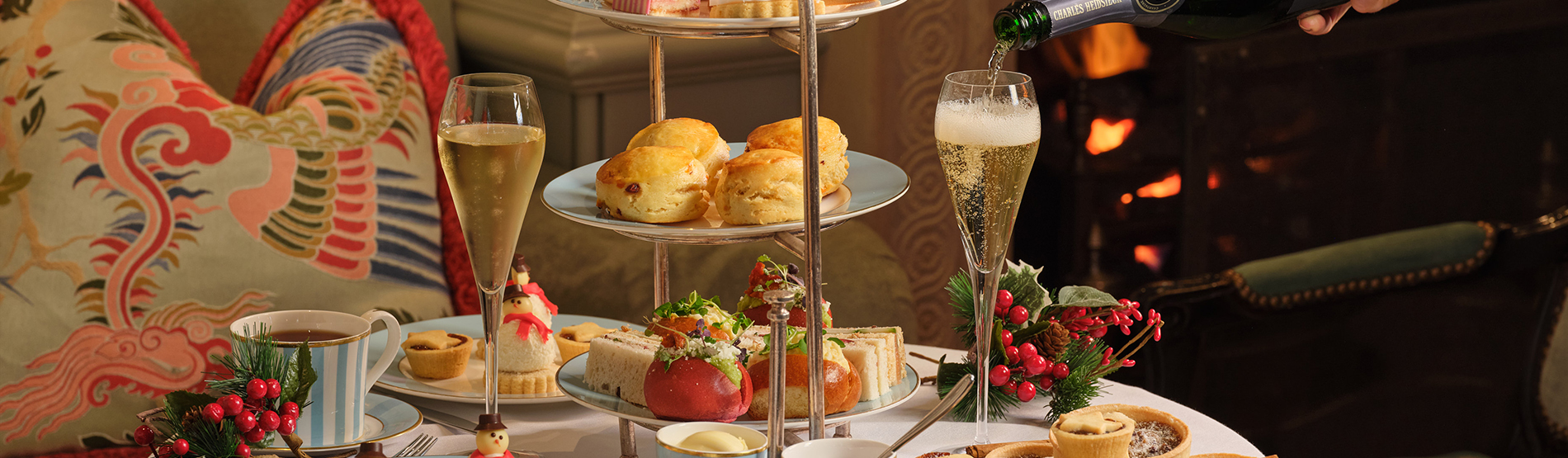 Festive afternoon tea at The Kensington Hotel, featuring a waiter pouring champagne into a flute amid a bright, elegant room decorated for the holidays.