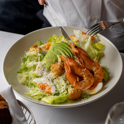 A close-up shot of an elegant woman enjoying a fresh gambas and avocado salad.