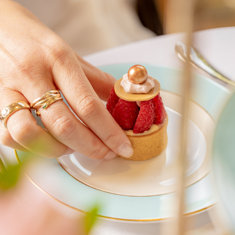 Close-up of a woman's hand taking a slice of gourmet raspberry layer cake topped with fresh berries from a British Afternoon Tea at The Kensington hotel