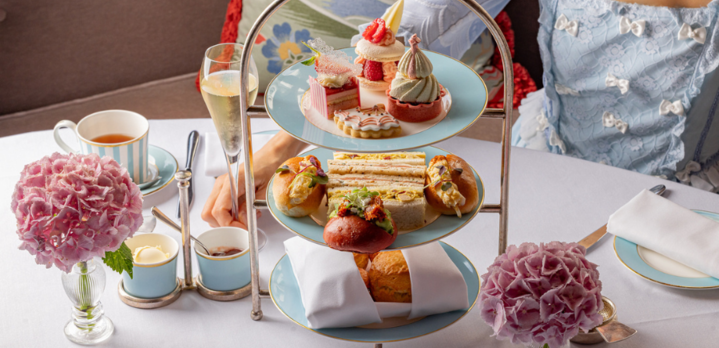An elegant afternoon tea setting at The Kensington hotel, featuring a three-tiered stand of treats, champagne, and a woman in a blue dress enjoying the moment.