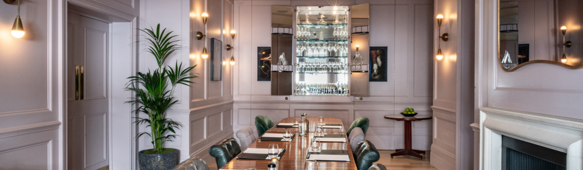 Elegant, light-filled room with a wooden table, leather chairs, and a blue velvet banquette under bay windows — The Study at The Kensington, ideal for private dining or meetings.