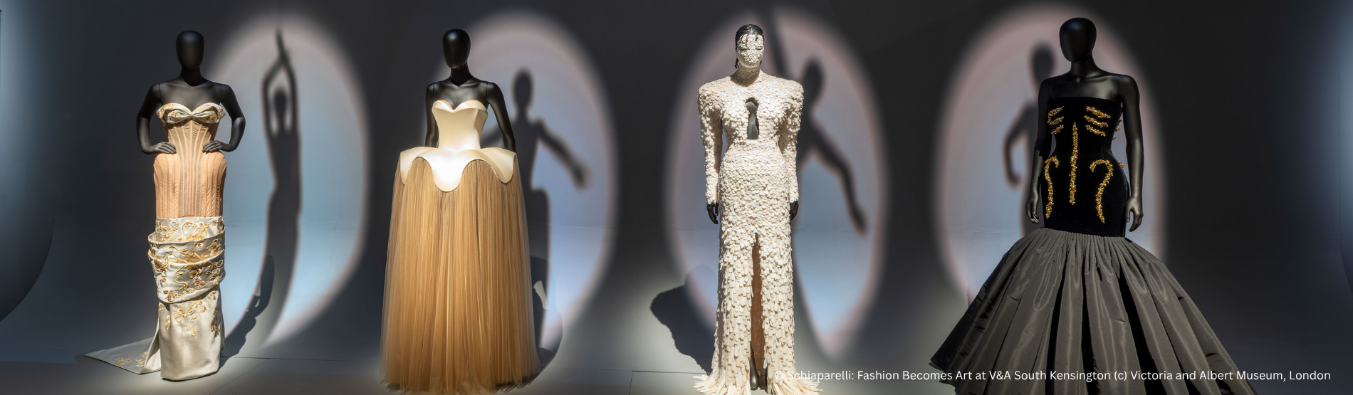 Museum display at the V&A featuring four mannequins in Schiaparelli-inspired fashion under a branded exhibition