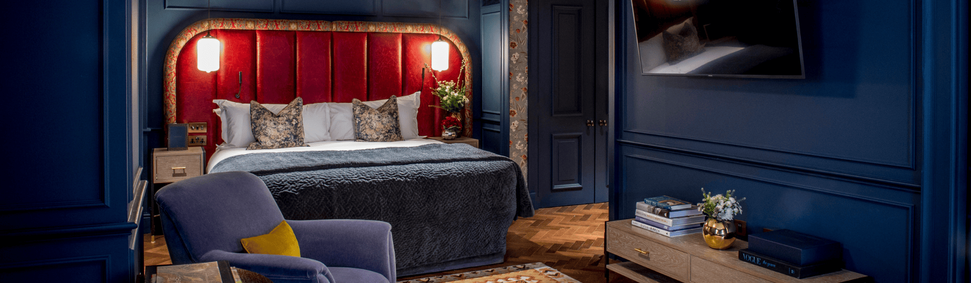 Luxury Studio Suite at The Marylebone Hotel. The room, decorated with blue and red accents for a winter theme, features a plush bed, a stylish armchair, and tv perfect for a luxury winter escape.