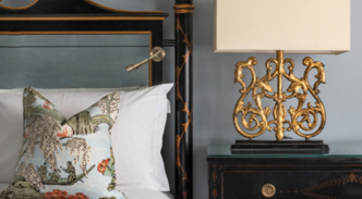 A twin room featuring a neatly made bed with white sheets and vibrant pillows, flanked by a dark black sideboard and complementary side lamp.