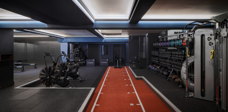 A clean and organized gym floor at The Third Space with rows of neatly arranged dumbbells and two stationary bicycles.