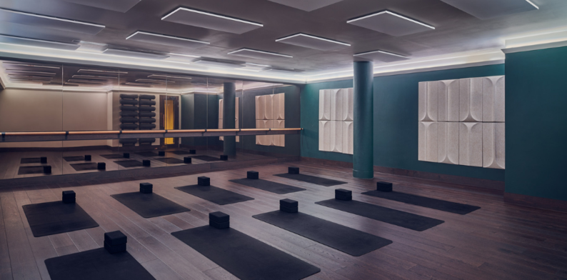 A yoga class at The Third Space. The studio has a mirror wall, yoga mats ready for a session, and a calming, dimmed-light atmosphere.