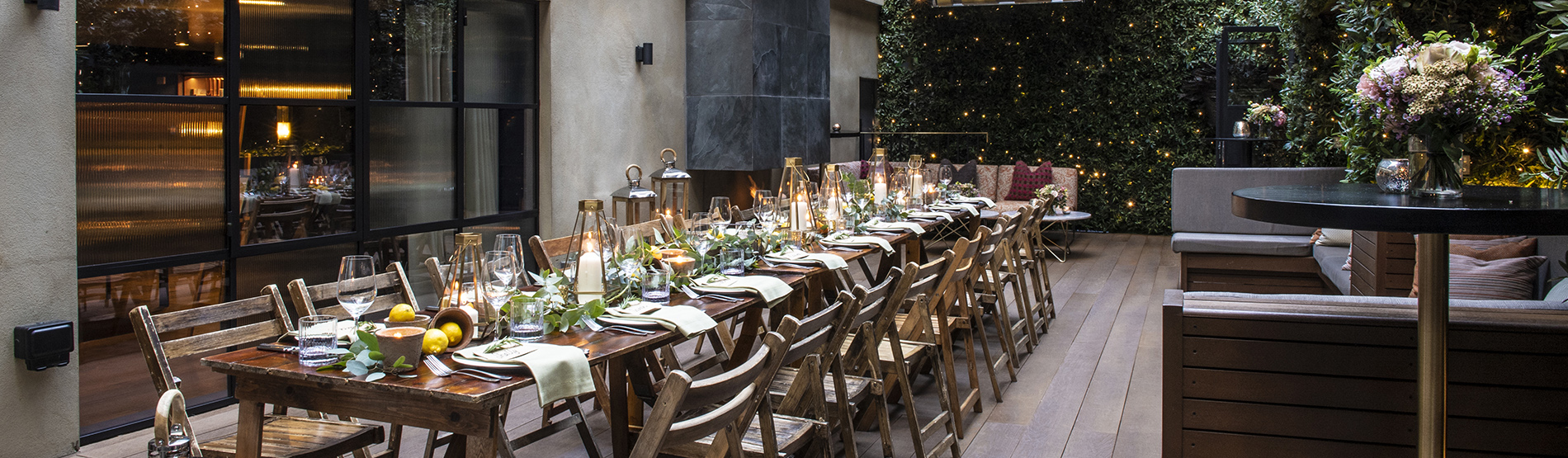 A beautifully arranged long dining table in the garden terrace at The Marylebone, styled with fresh lemons, lush green foliage, and flickering candles under soft outdoor lighting