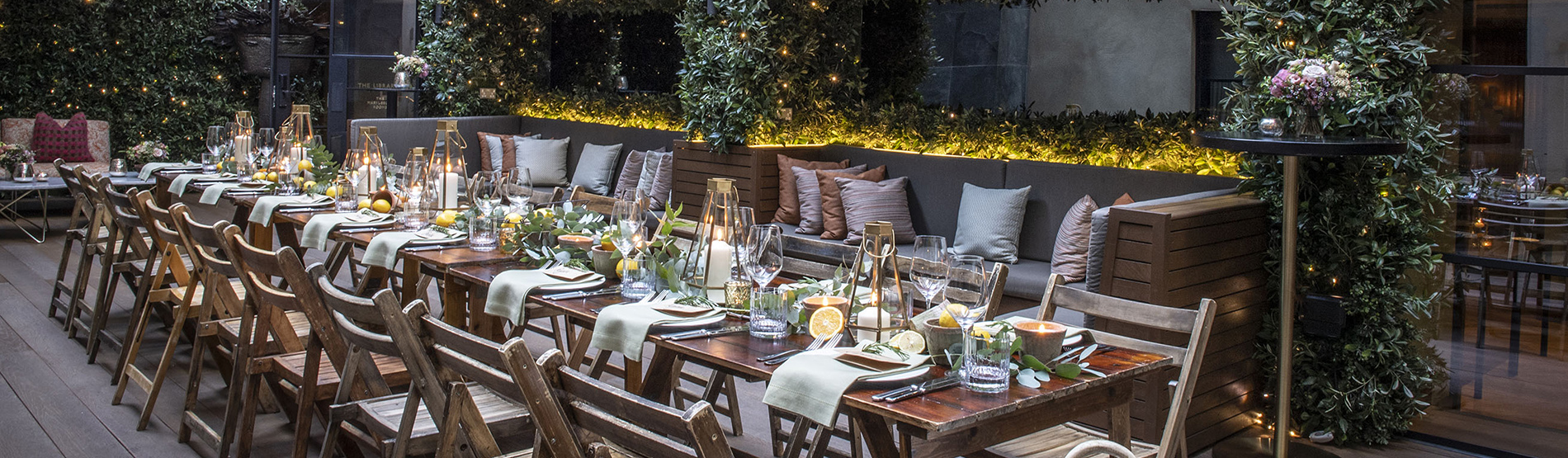 A beautifully arranged long dining table in the garden terrace at The Marylebone, styled with fresh lemons, lush green foliage, and flickering candles under soft outdoor lighting