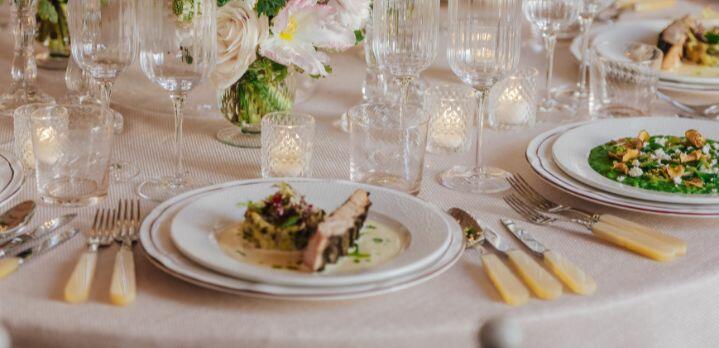 Close-up of a wedding reception table setting with plated dishes, including a fish main course served. The table is elegantly dressed with glassware and cutlery, reflecting a refined dining experience.