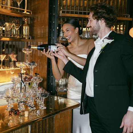 A smiling couple pours a champagne pyramid at their private wedding reception inside The Marylebone Hotel.