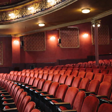 Interior view of a historic Cork theatre featuring rows of empty red velvet seats and tiered balcony levels.