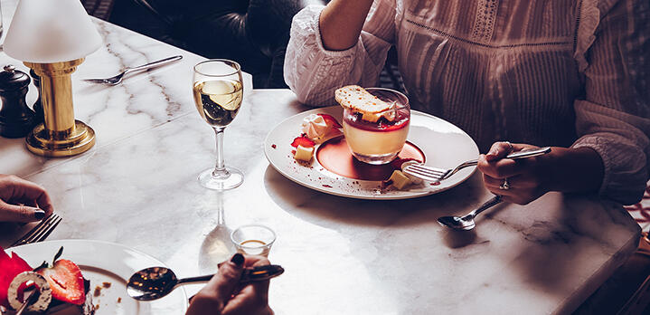 Close-up of two ladies enjoying dessert with glasses of chilled white wine at a marble table in the River Grill, The River Lee.