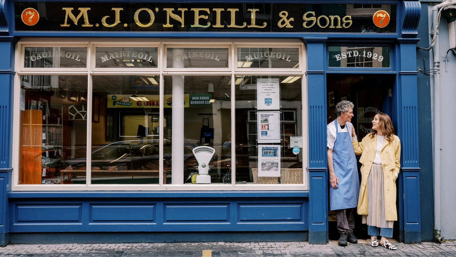 Louise O'Neill smiling with her father in front of a blue-fronted butcher shop in Cork.