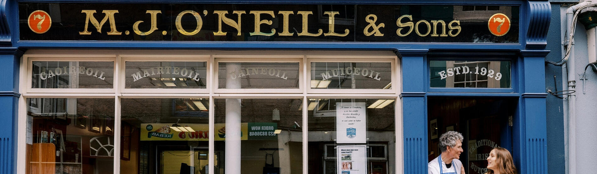 Louise O'Neill smiling with her father in front of a blue-fronted butcher shop in Cork.