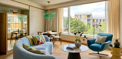 Luxury suite at The River Lee Hotel featuring a light blue round sofa, coffee table, armchair, and large windows with a scenic view.