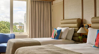 A Deluxe King River View room at The River Lee Hotel, showcasing a spacious king bed and a seating area with two signature blue armchairs