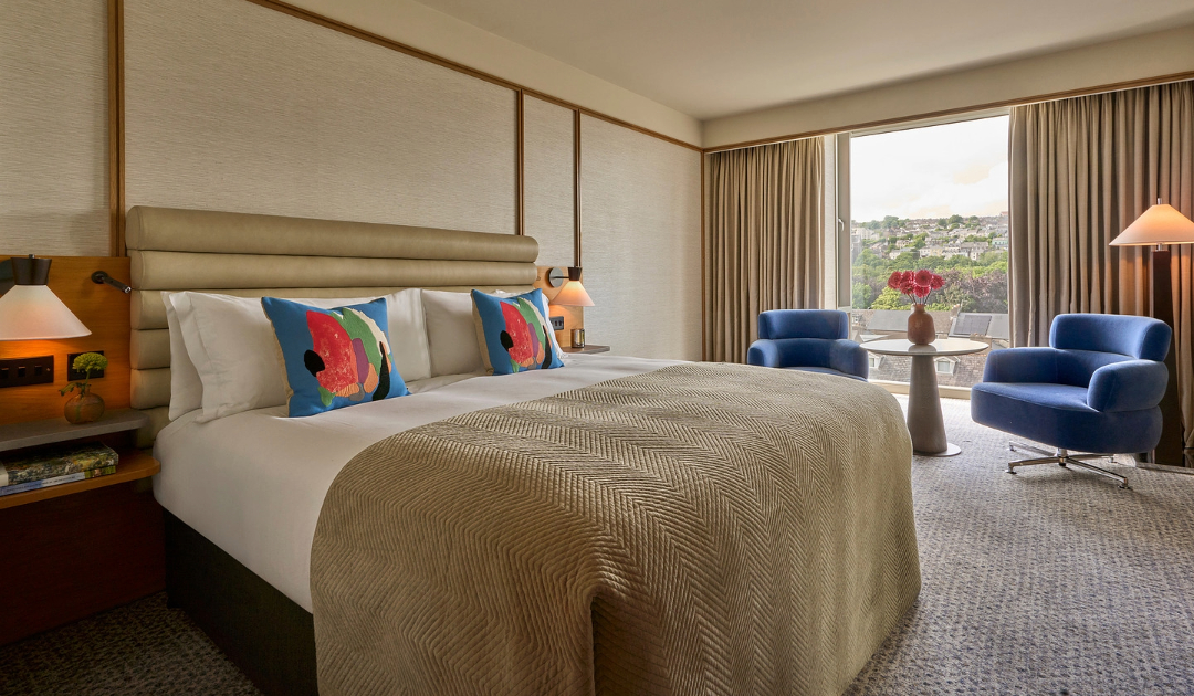 Deluxe River View Room at The River Lee, showcasing a king bed and a cozy seating area complete with two vibrant blue armchairs.