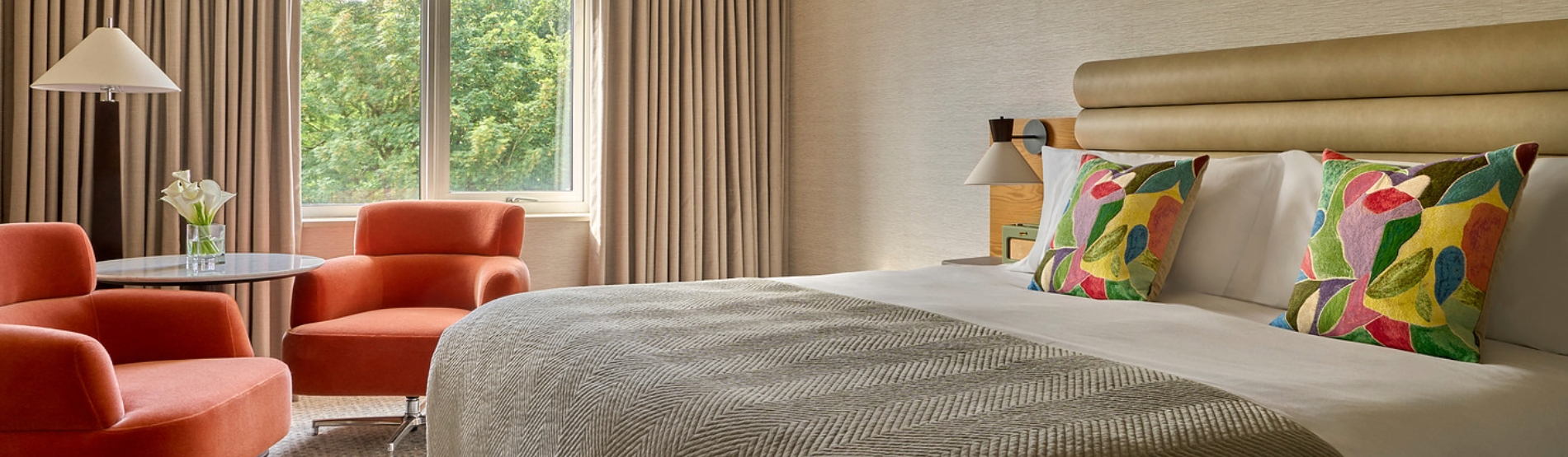 The Classic Room at The River Lee Hotel, Cork, features a comfortable double bed, two vibrant orange armchairs, a small table, and warm lamp lighting, creating a stylish and relaxing retreat.