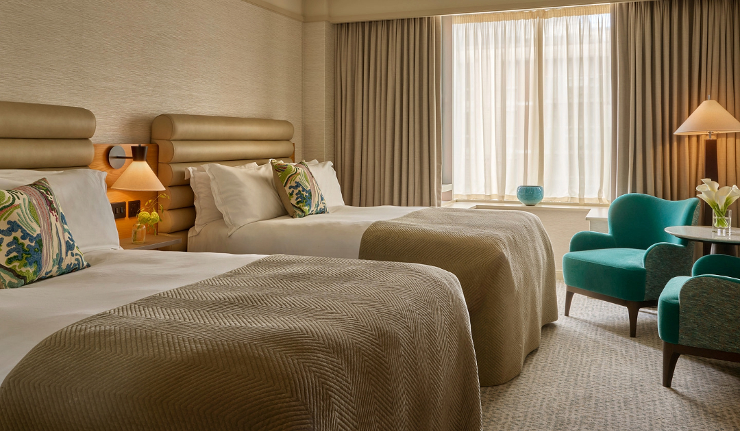 Classic Room at The River Lee Hotel in Cork featuring two double beds, a lamp, and two turquoise armchairs with a small coffee table set in front of a large window.