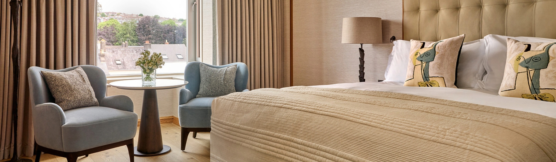 Luxury Suite in The River Lee hotel featuring the king bedroom with two armchairs placed in front of large windows.