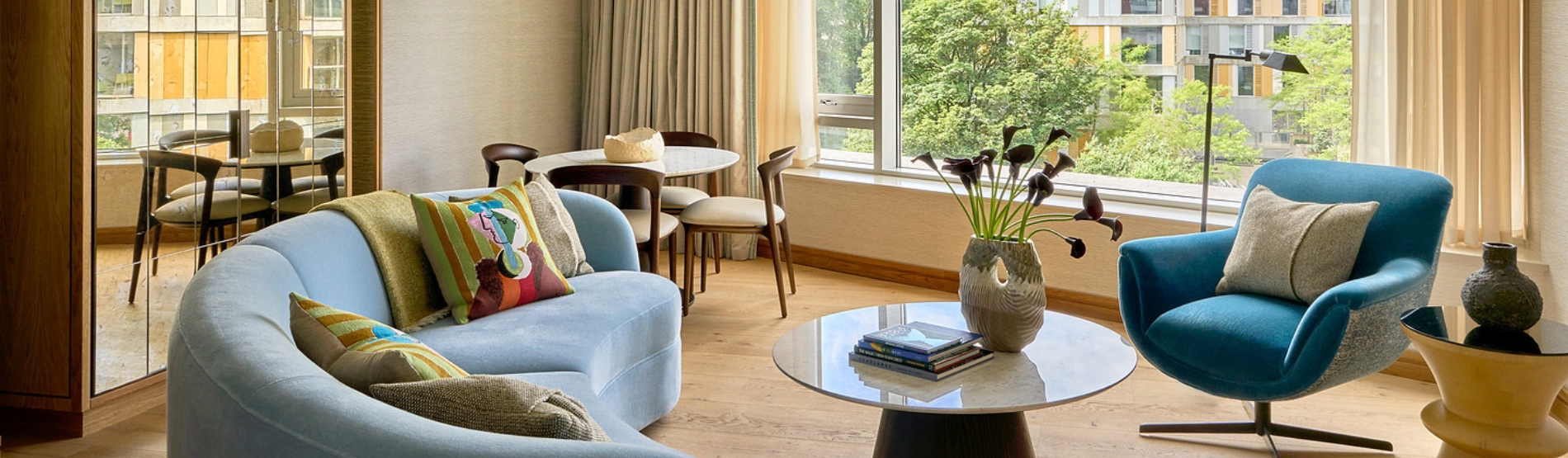 Sunlit luxury suite living area overlooking Cork, showcasing a contemporary sofa and armchair setup with beautiful flowers on the coffee table by the large windows.