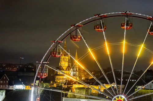 A festive Ferris wheel illuminated against the night sky, with a church adding to the holiday scene in Cork city.