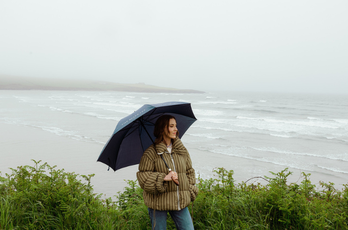 Louise O'Neill holding an umbrella by the sea on a rainy day during a 48-hour West Cork experience.