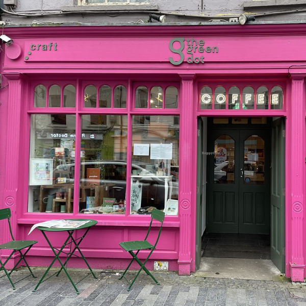 The Green Dot shop exterior with a distinctive pink facade, featuring a small table placed outside the entrance.