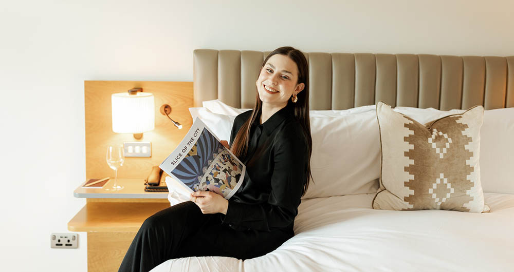 Jo sitting on the bed reading our Slice of the City magazine