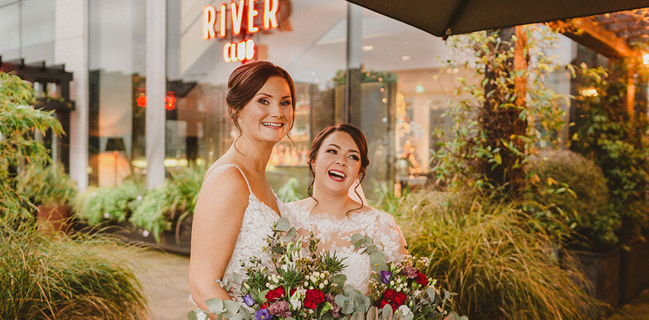 Sinead & Laura with colourful bouquets of flowers outside The River Club