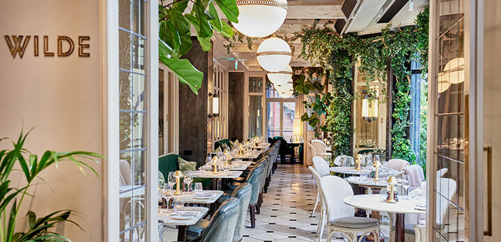 Bespoke dining at WILDE: Lush greenery and glowing warm lights frame a beautifully set restaurant floor, perfect for a refined evening out.