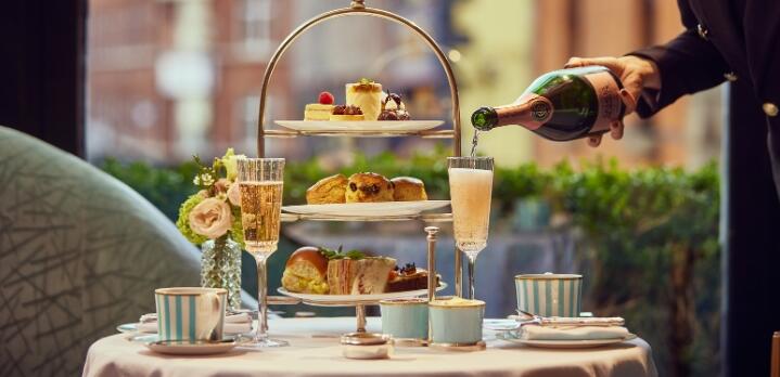 A luxury afternoon tea service at The Gallery, featuring a tiered stand of artisanal pastries and sandwiches as a waiter pours sparkling champagne into elegant flutes