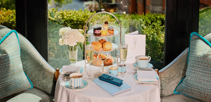 A luxury afternoon tea service at The Gallery, featuring a tiered stand of artisanal pastries and sandwiches as a waiter pours sparkling champagne into elegant flutes