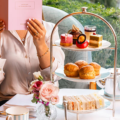  An exquisite afternoon tea spread at The Gallery in The Westbury hotel, featuring a three-tiered stand laden with an assortment of pastries, scones, and sandwiches and a lady looking in the menu.