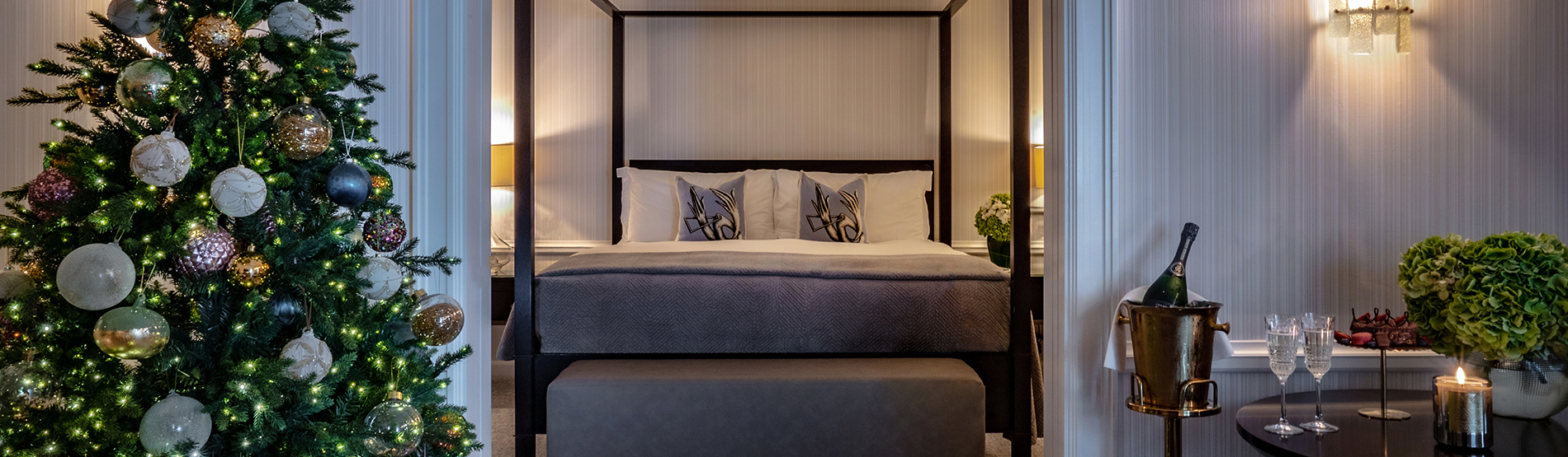 Luxurious suite at The Westbury Hotel, featuring a four-poster bed, a beautifully decorated Christmas tree, and a small table set with a bottle of champagne and two glasses.
