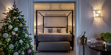 Luxurious suite at The Westbury Hotel, featuring a four-poster bed, a beautifully decorated Christmas tree, and a small table set with a bottle of champagne and two glasses.