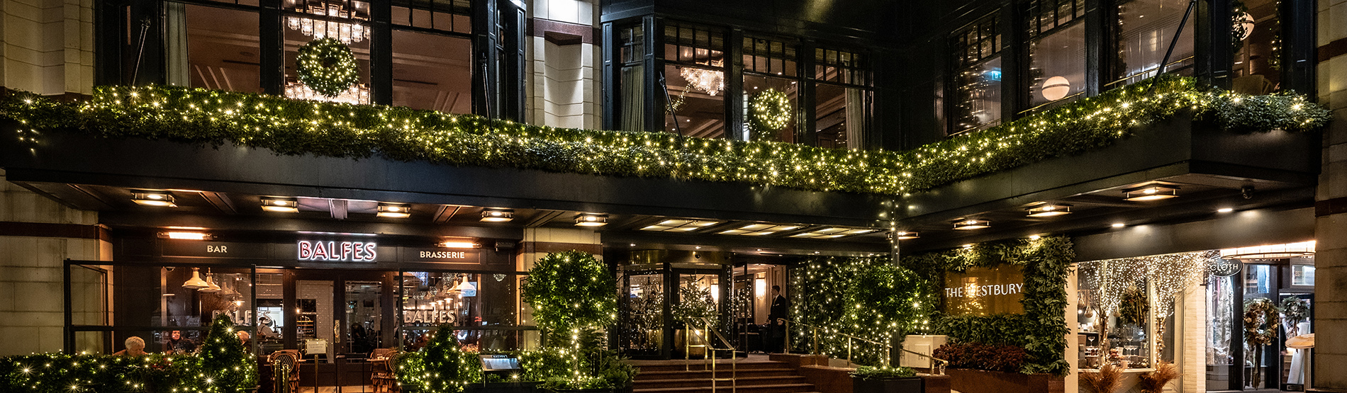The exterior view of The Westbury hotel at night, adorned with festive Christmas lights and wreaths on the windows.