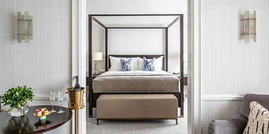 Luxurious suite at The Westbury hotel, featuring a four-poster bed. A table is set with macarons and two glasses of Champagne.