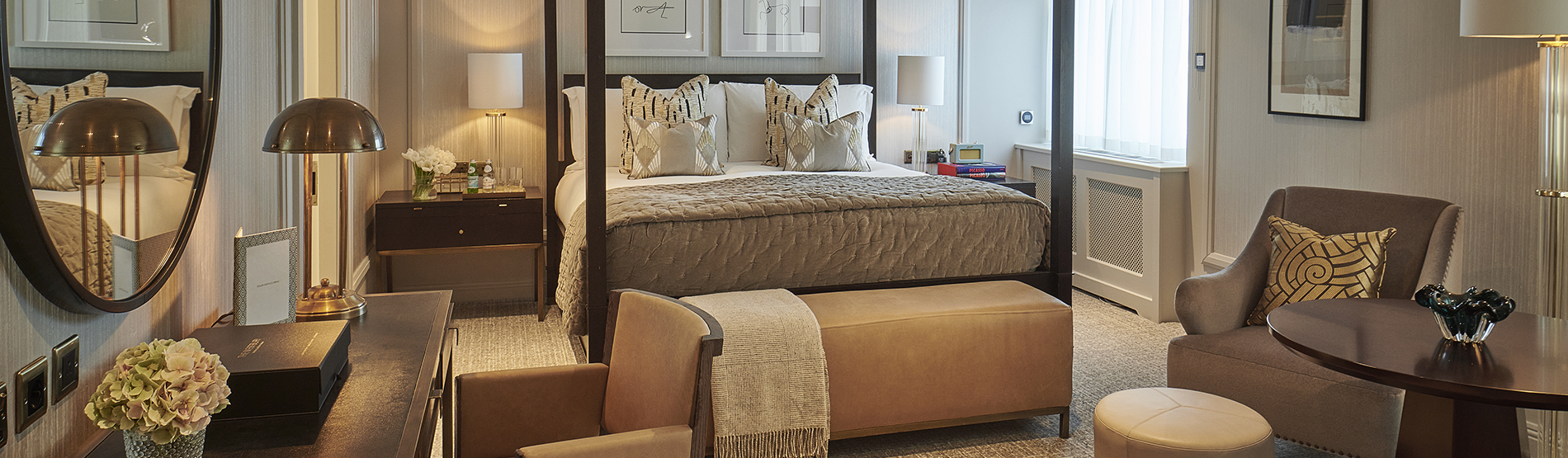 Studio suite at The Westbury hotel featuring a four-poster bed, an armchair with a side table, and fresh flowers on a dressing table.