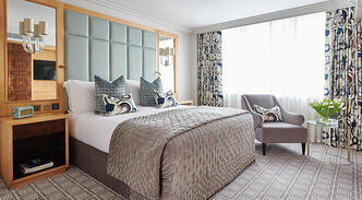 Luxury suite master bedroom at The Westbury, showcasing contemporary grey and light blue interiors, a king-size bed, a stylish armchair, and fresh floral accents