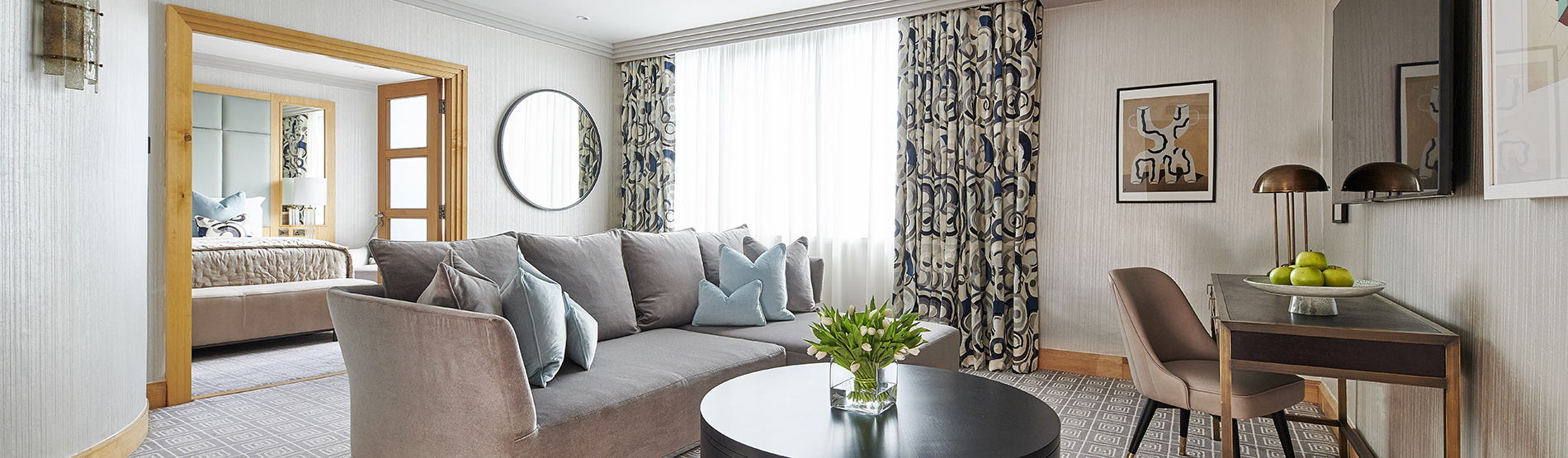 The spacious living room of a Luxury Suite at The Westbury Hotel, featuring sleek, low-slung sofas, and elegan artwork. 