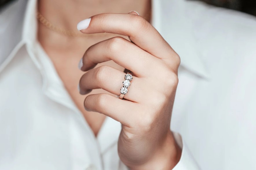 A luxury jewelry display featuring three radiant diamond rings by Dublin-based jeweler Brian Jacobson. The hand is positioned to catch the light, highlighting the diamond's clarity and cut against a clean, minimalist background, embodying the bespoke elegance found at Jacobson Diamonds.