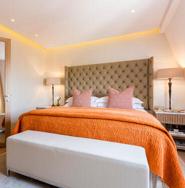 bedroom with bed with orange throw and pink cushions